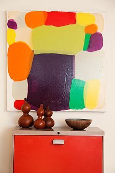 an abstract painting on the wall above a red cabinet