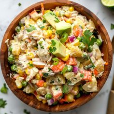 a wooden bowl filled with chicken salad and garnished with avocado, cilantro, corn, carrots, green onions