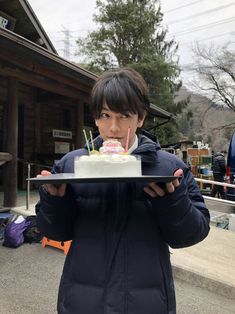 a woman holding a tray with a cake on it in front of her face and looking at the camera