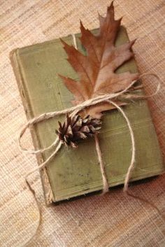 an old book with a leaf tied to it on a table next to some twine