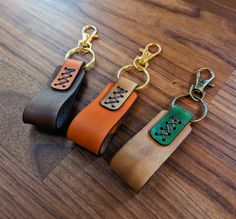 three leather keychains are sitting on a wooden surface, one is orange and the other is green