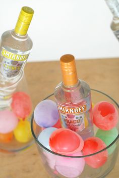 a bottle of vodka sitting on top of a glass bowl filled with colorful candy eggs