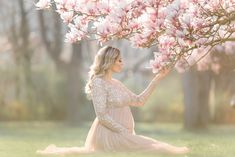 a woman in a dress sitting under a tree with pink flowers on it's branches