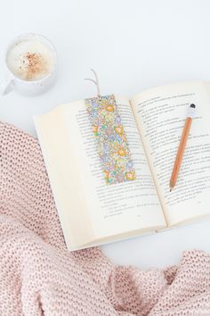 an open book on top of a blanket next to a cup of coffee and a pencil