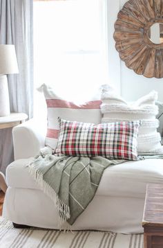 a white couch with pillows and blankets on it in front of a window that has a sunburst