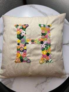 a pillow with the letter h embroidered on it, sitting on a table next to a chair