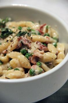 a white bowl filled with macaroni and cheese covered in meat, vegetables and seasoning