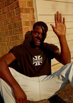 a man sitting on the ground with his hand up in front of him and wearing a brown shirt