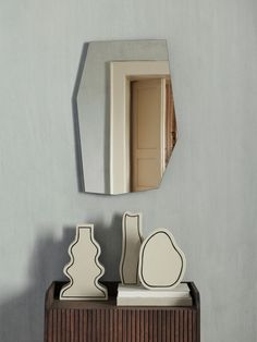 a mirror and some vases on a wooden shelf in front of a gray wall