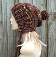 Knit Hat Style: Charlotte Slouchy Beanie - a chunky knit slouchy hat with pom pom and braided ties, for women, men and teens. Color: This sample hat is shown in Sequoia, a mix of browns, golds and rust. Sizes: One size fits average teen or adult head size of 20" to 23" (50.5 cm to 58 cm). Fiber Content: 80% acrylic, 20% Wool Characteristics: Chunky, very soft, warm and cozy.  Care Instructions: Hand wash, dry flat.  Every item from Pixiebell is handmade and knit or crocheted to order, unless oth Knit Slouchy Hats, Brown Beanie, Hat With Pom Pom, Flap Hat, Crochet Hat For Women, Brown Hat, Chunky Knit Hat, Ear Flap Hats, Mens Hat