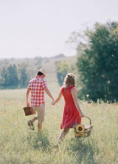 a man and woman holding hands walking through tall grass with baskets in each hand, on a sunny day