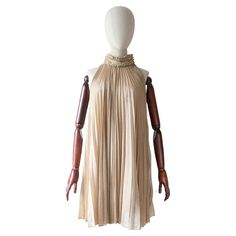 An iconic beauty to behold, this original 1960's gold lurex dress, set off by accordion pleats and gold braiding along the neckline, is a true piece of fashion history. The high collared neckline, fastens along the left hand side with press studs and hook and eye fastenings. The collar is accented by pleated and gathered edgings along the top and bottom, framing a simple gold lurex panel. The elegant racer back cut of the dress sets off the sleeveless design, which draws the eye to the magnifice 1960s Cocktail Dress, Rich Auntie, Vintage 1930s Dress, Iconic Beauty, Lurex Dress, Accordion Pleats, Bolero Dress, 1930s Dress, Dress Sets