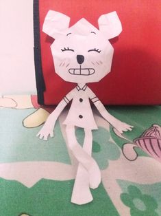 a paper doll is standing next to a red bag