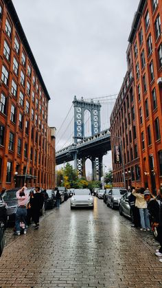 people are standing on the sidewalk in front of some tall buildings with a bridge above them