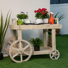 a wooden cart filled with potted plants sitting on top of grass next to a building