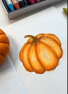 a drawing of a pumpkin on paper next to some crayons