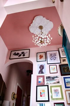 a hallway with pink walls and framed pictures on the wall, including a chandelier