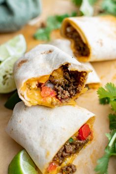 two burritos cut in half on a cutting board with cilantro and lime