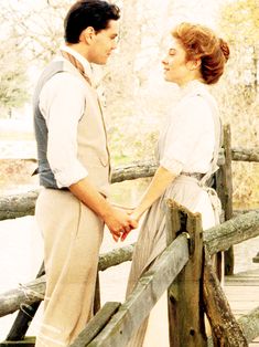 a man and woman standing on a bridge near each other, looking at each other