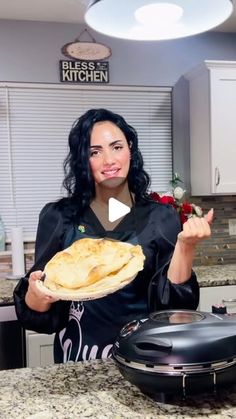 a woman holding a plate with food on it in a kitchen next to an electric skillet