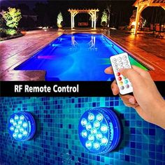 a person holding a remote control in front of a swimming pool with lights on it