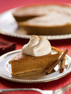 a slice of pumpkin pie with whipped cream on top and cinnamon sticks next to it