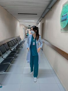 a woman in scrubs is walking down the hallway with her hand on her hip