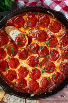 a pepperoni pizza in a cast iron skillet on a table with bread and parsley