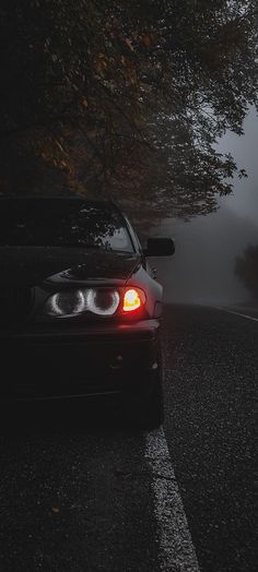 a car is parked on the side of the road in the dark with fog behind it