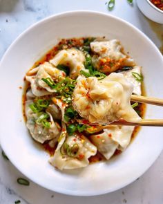 a white bowl filled with dumplings covered in sauce and garnished with green onions