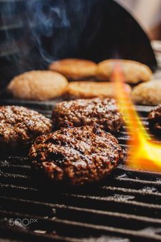 burgers and hamburger patties cooking on an outdoor grill with flames coming from them