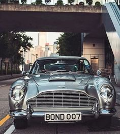 an old silver car is parked on the side of the road in front of a bridge