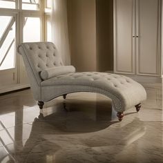 a white chaise lounge chair sitting on top of a tile floor next to a window