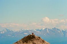 two people sitting on top of a mountain with snow capped mountains in the background,