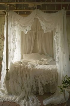 an old fashioned bed with white linens and lace on the canopy, in a bedroom