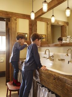 two young boys standing in front of a bathroom sink and looking at each other's reflection