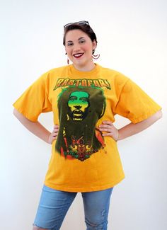 This is an awesome 90s vintage Bob Marley t-shirt with a huge vinyl graphic of the reggae artist's face in green and black on a yellow-orange heavy cotton tee. It says "Rastafari" across the top in block letters and "Bob Marley" across the bottom. The shirt is in well loved, clean, distressed vintage condition with a 2 inch tear at the edge of the crew neck collar. There are yellow, black and green paint splatter marks around the front but they are actually part of the vinyl graphic and are orig Vintage Festival T-shirt With Short Sleeves, 90s Graphic Print Festival Tops, Vintage Short Sleeve T-shirt For Festival, Vintage Short Sleeve Festival T-shirt, 90s Style Screen Print T-shirt, 90s Crew Neck T-shirt For Music Festival, 90s Style Crew Neck T-shirt For Music Festival, Yellow Short Sleeve Grunge T-shirt, Retro Screen Print T-shirt For Festivals