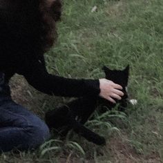 a woman petting a black cat in the grass