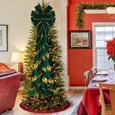 a decorated christmas tree in the middle of a dining room with red walls and chairs