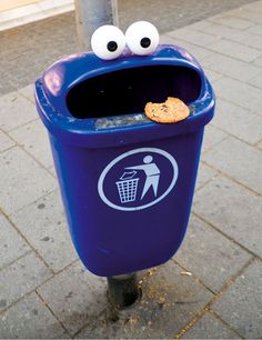 a blue trash can with googly eyes and a cookie in it