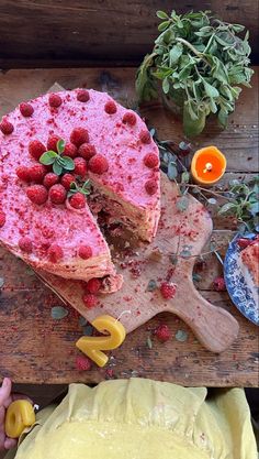 a person cutting a cake with raspberries on it and other desserts nearby