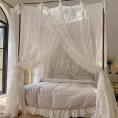 a bed with white sheets and curtains on it's headboard, in front of an arched window