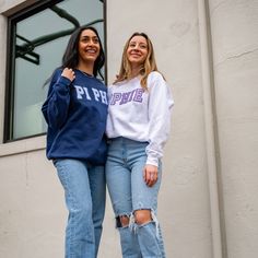 two young women standing next to each other in front of a building wearing sweatshirts and ripped jeans