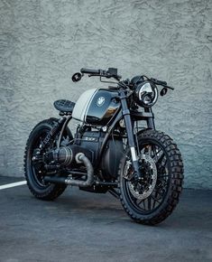 a black and white motorcycle parked in front of a gray wall with no one on it