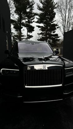 a black rolls royce parked in front of some trees