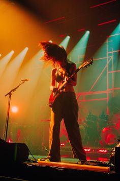 a woman standing on stage with her guitar in front of the microphone and lights behind her