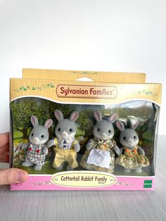 a hand is holding two toy rabbits in a box with the packaging on it's side