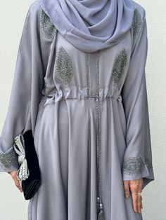 A premium addition, the Grey Laila Umbrella Abaya with a combination of applique and stoneworks, made with premium quality nida. Perfect for occasions all year round. Its inner tassel belt can be adjustable to get a more desired look. Suitable for special occasions like all year round  Closed Abaya Fabric: 100% Nida ( Soft & Lightweight) Beautiful flow gives an elegant look Embroidery details on sleeves, chest, and lower panel of the abaya. Hijab: Included Belt: Tassel, included The model is a U Dubai Abaya, Tassel Belt, Dresses Elegant, Abaya Dress, Embroidery Details, Look Plus, Elegant Dresses, Dress Clothes For Women, Modest Fashion