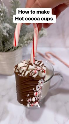 someone is holding two candy canes over a hot cocoa cup with marshmallows