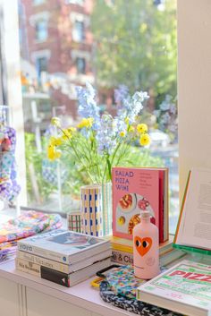 a window sill filled with books and flowers next to a vase full of flowers